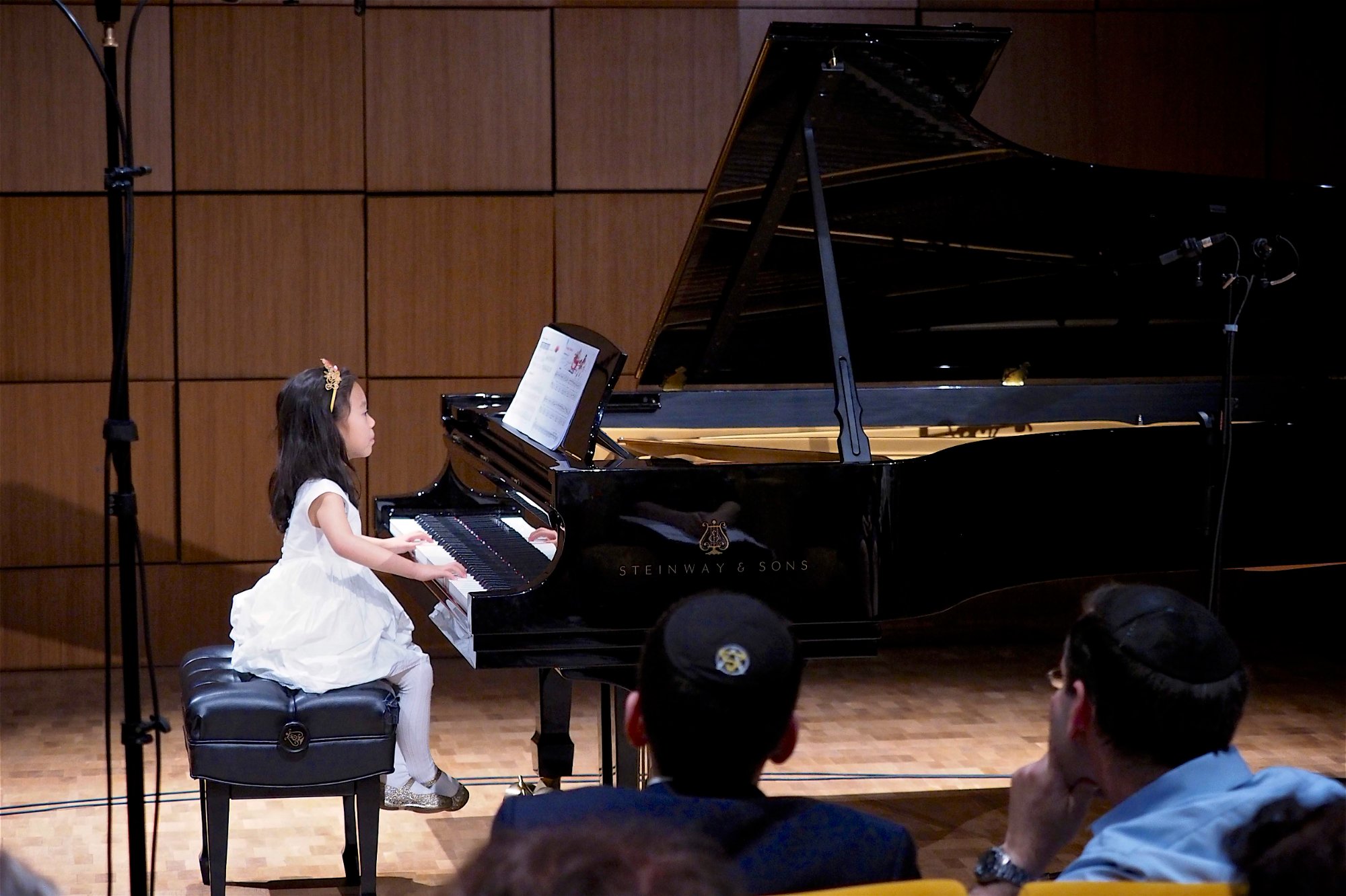 Young student in white dress performing at Steinway grand piano